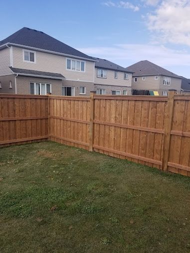 A wooden fence in a backyard with houses in the background.