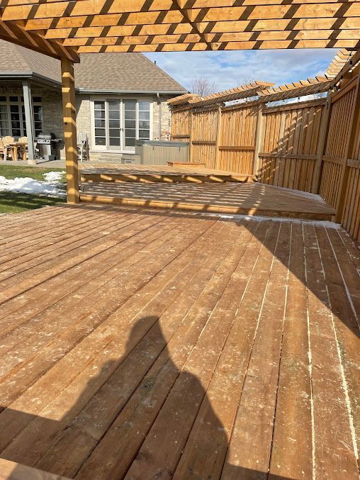 A wooden deck with a pergola and a house in the background.