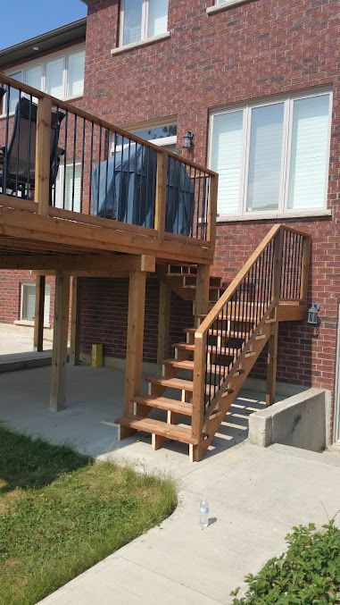 A wooden deck with stairs leading up to it in front of a brick house.