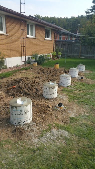 A row of concrete pillars are sitting in the dirt in front of a house.