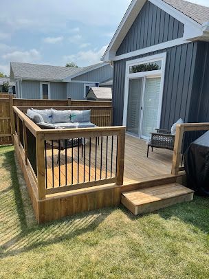 A wooden deck with a couch and chairs in front of a house.