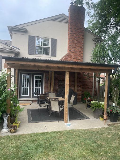 A patio with a table and chairs under a pergola in front of a house.