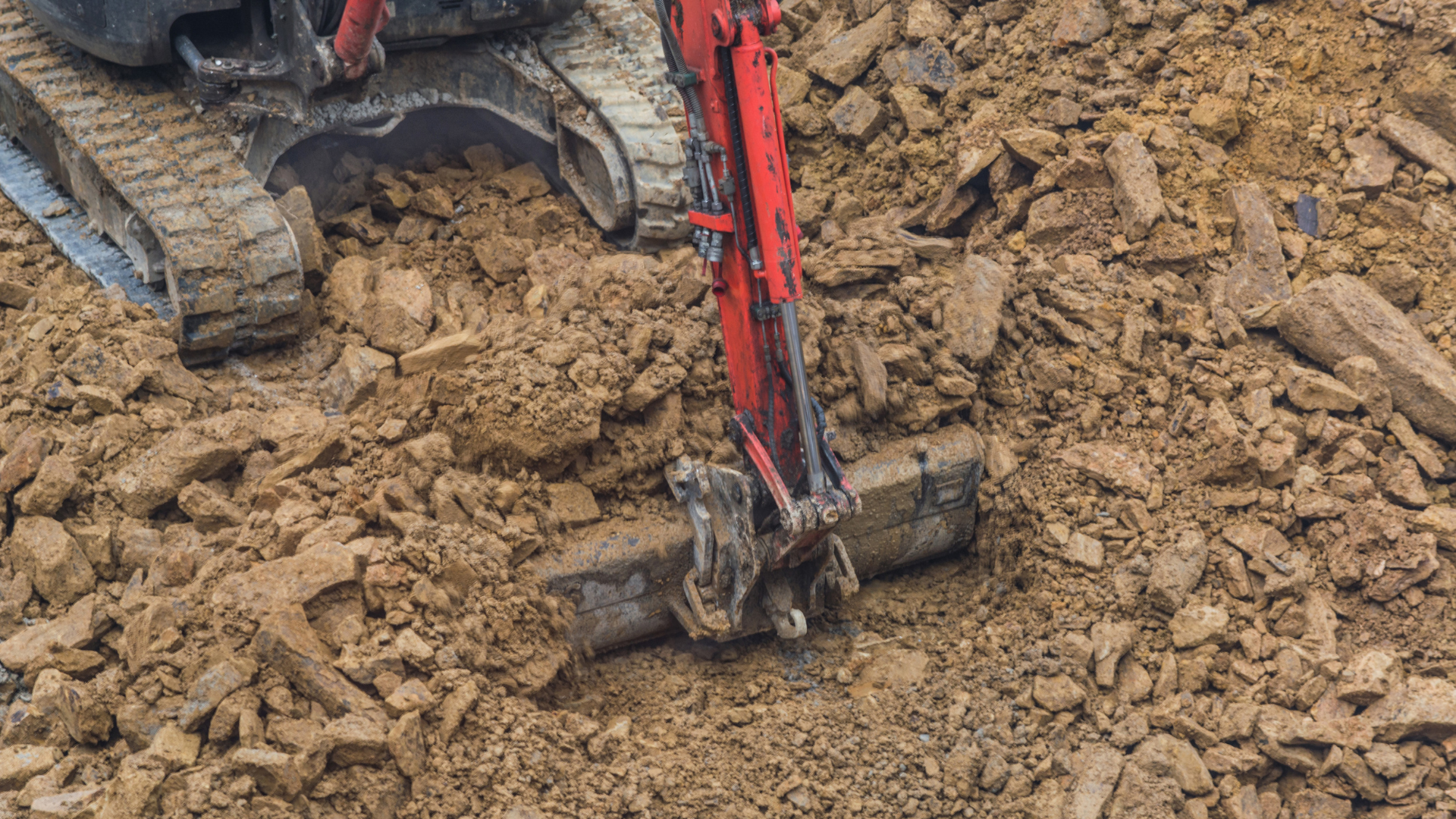 A red excavator is digging a hole in the dirt.