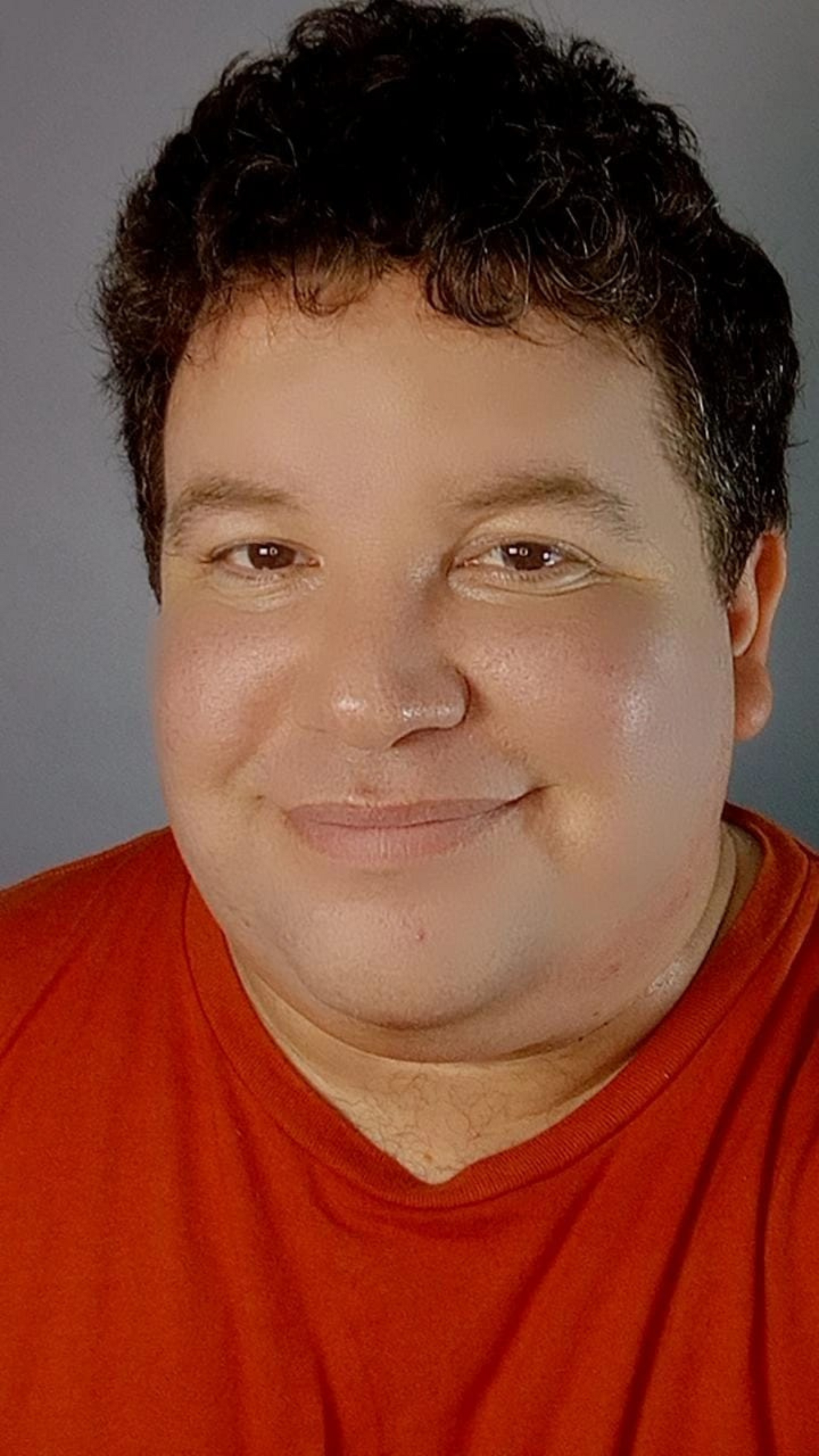 Hombre con cabello castaño rizado, vestido con una camisa naranja, sonriendo a la cámara.