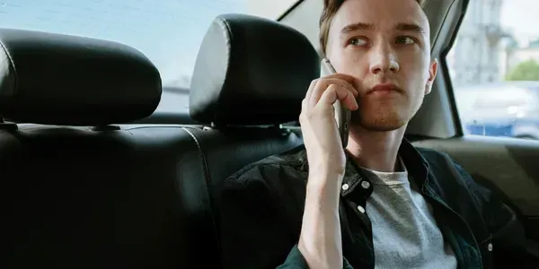 A man is sitting in the back seat of a car talking on a cell phone.