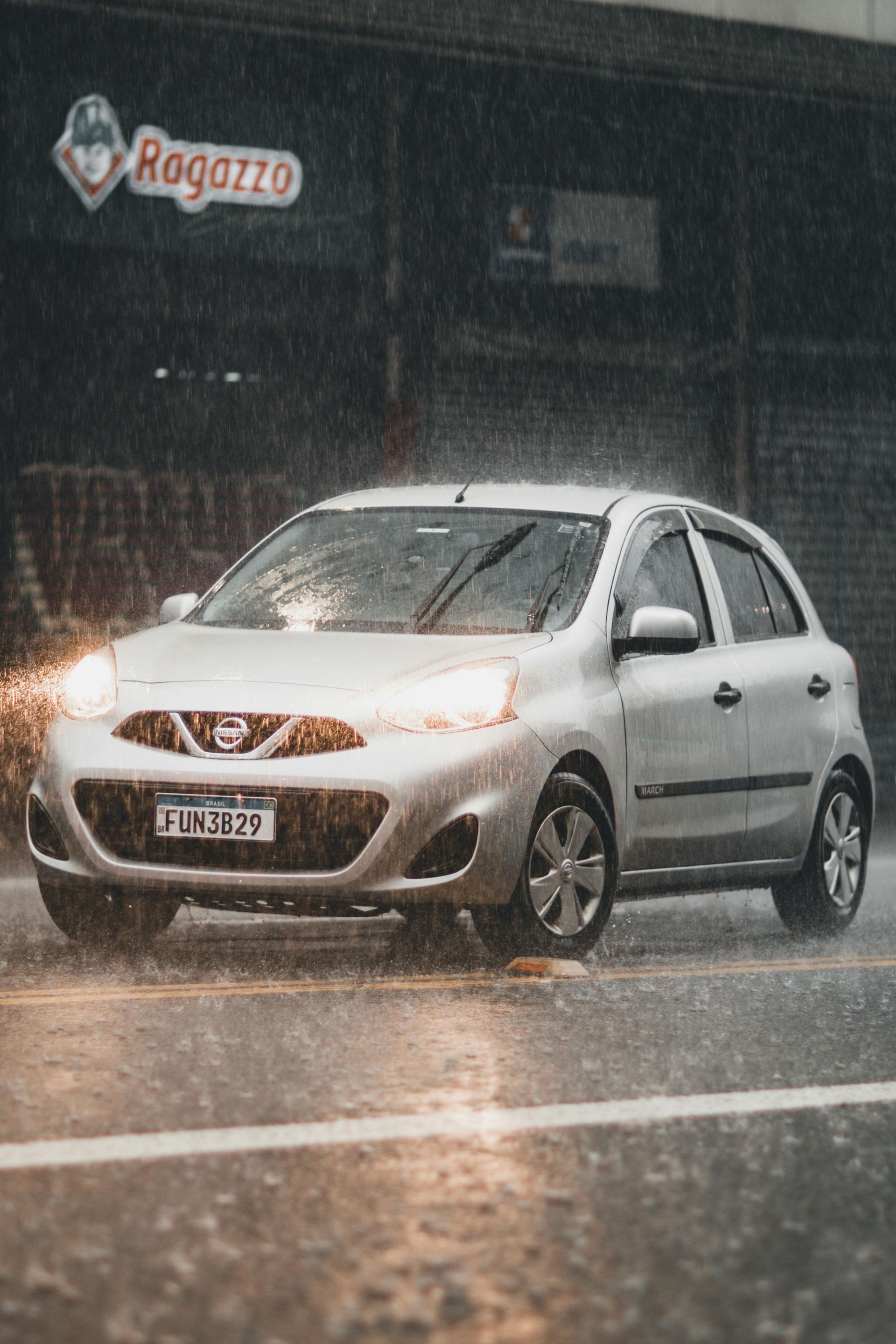 Silver hatchback driving in heavy rain on a wet road at night