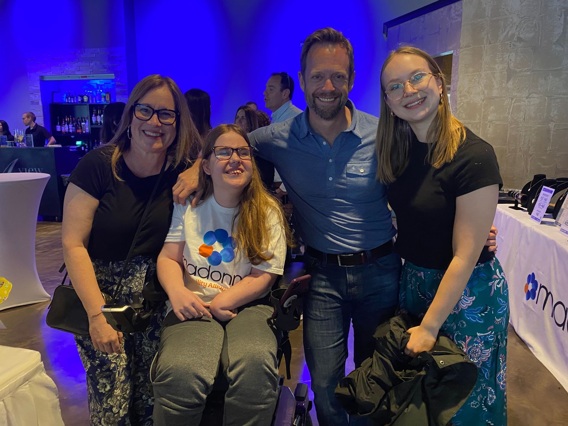Four people pose for a photo in a room with blue lighting. Two women, one in a wheelchair, and a man smile.