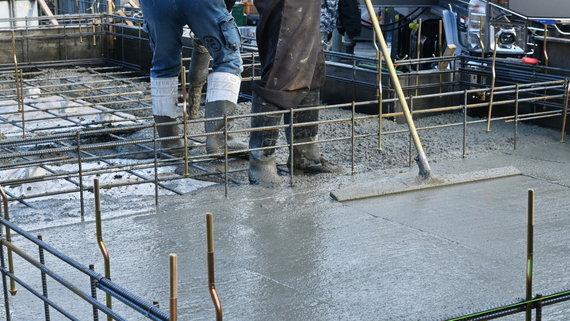 Workers pouring wet concrete over rebar at a construction site