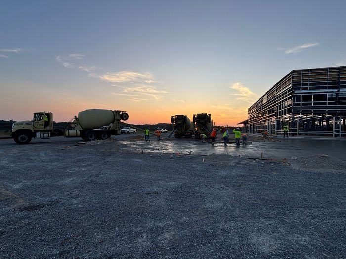 Construction workers smoothing wet concrete at a building site with a mixer truck in the background