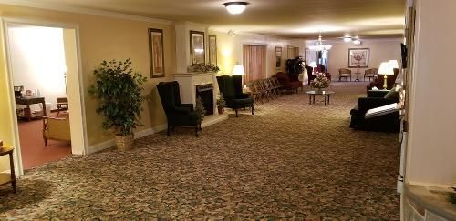 Well-lit hotel lobby with patterned carpet, armchairs, and tables in a long hallway-like seating area
