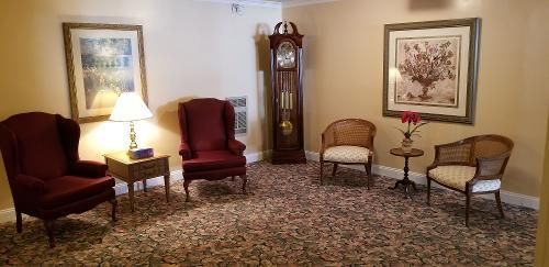 Elegant living room with four chairs, a floor lamp, grandfather clock, and framed artwork on patterned carpet