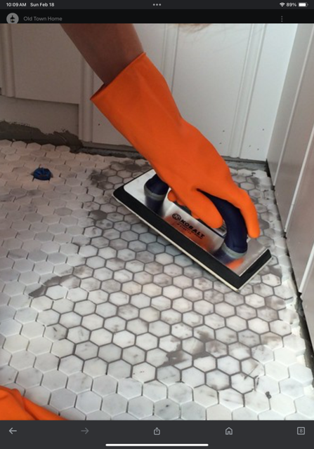 A person wearing orange gloves is working on a tile floor