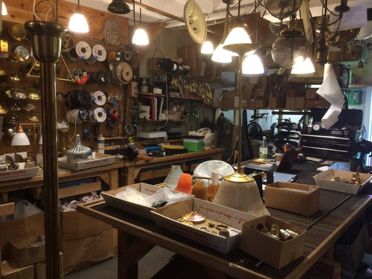 Workshop interior filled with tools, wires, lamps, and various objects on workbenches and shelves.
