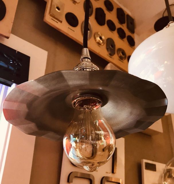 A pendant light fixture with a decorative, fluted metal shade and exposed lightbulb hanging indoors.