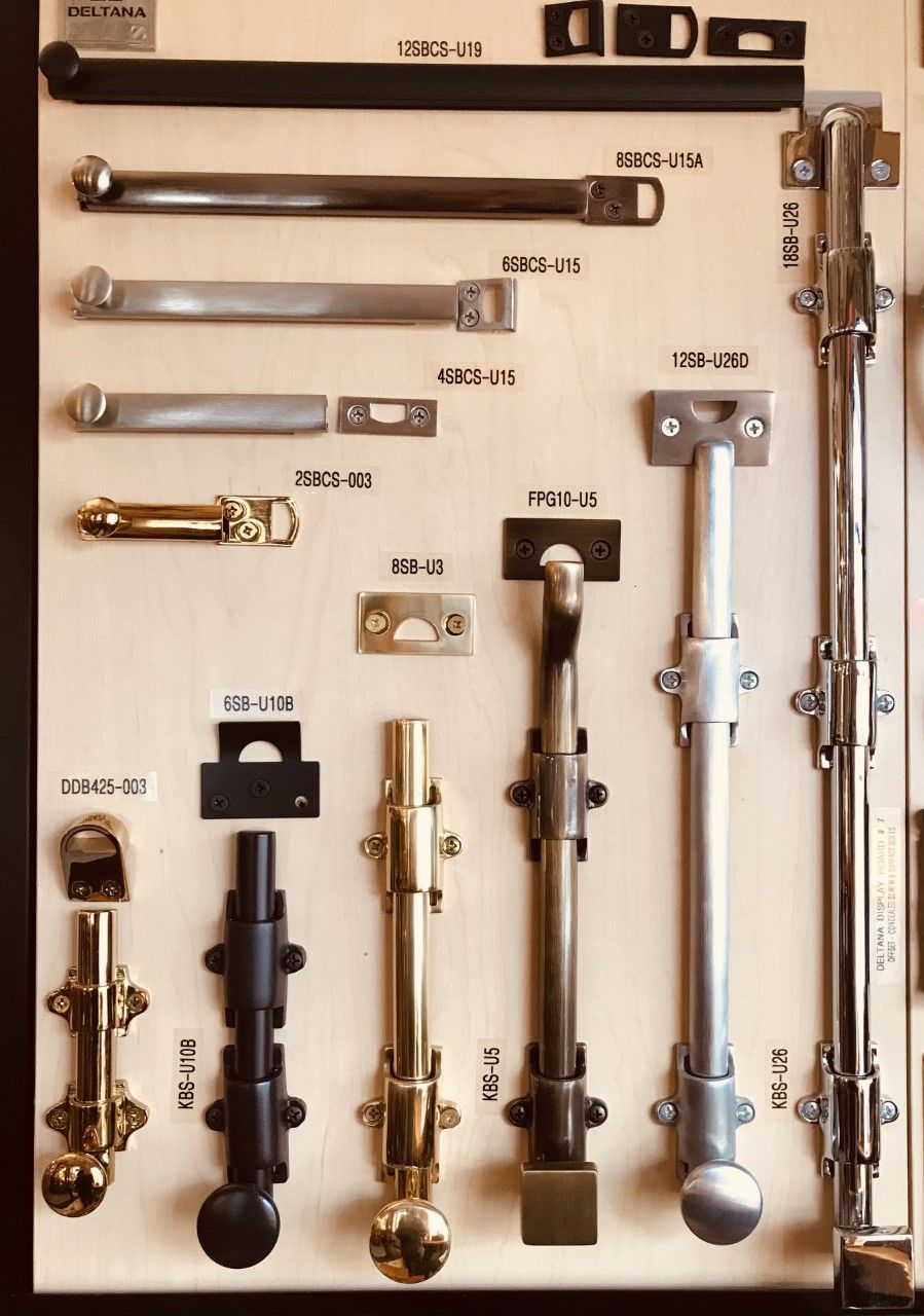 Display of various metal door bolts in different styles and finishes on a wooden board.