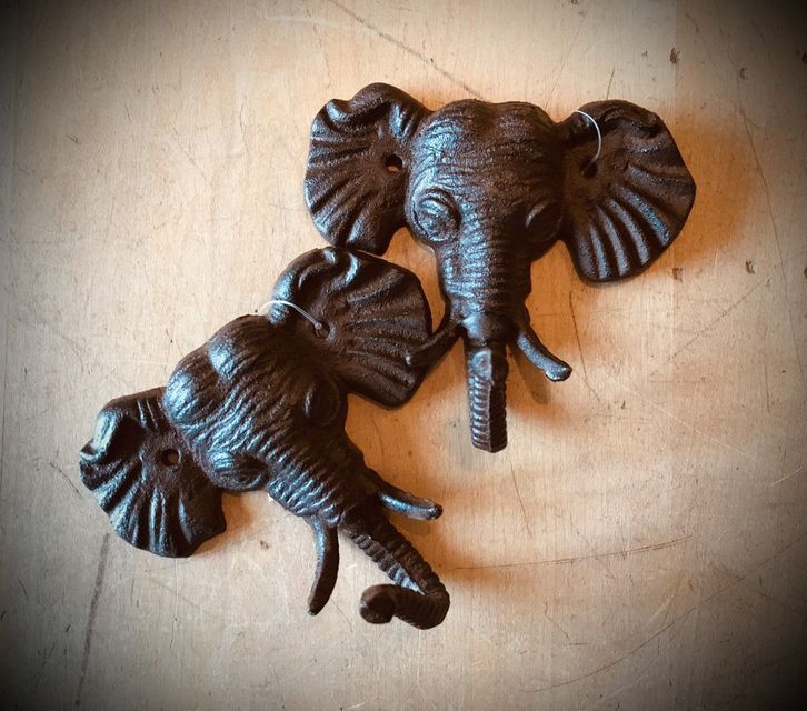 Two weathered cast-iron elephant head sculptures on a wooden surface.