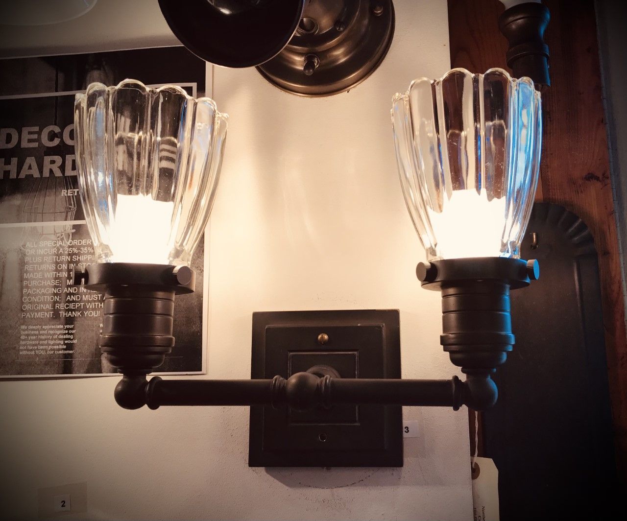 Two-bulb wall sconce with clear, fluted glass shades and bronze hardware, illuminating a wall.