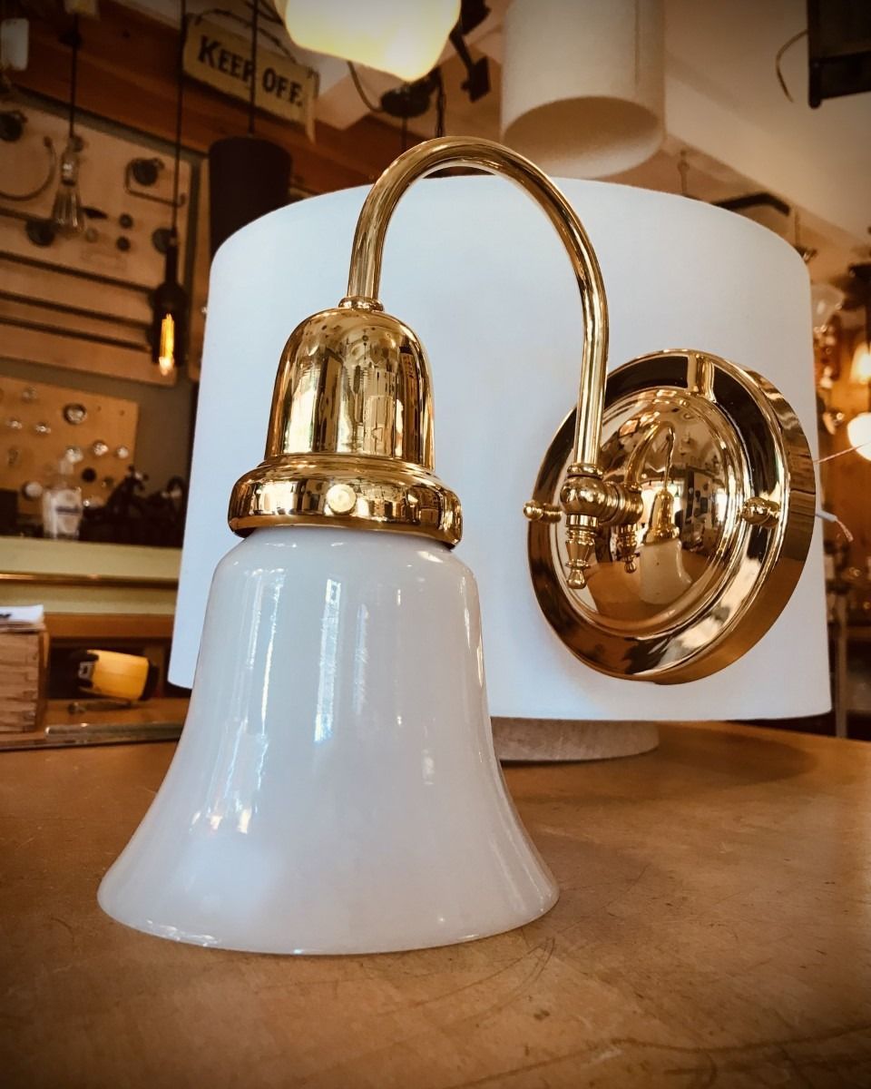 White glass bell-shaped wall lamp with gold fixtures, on a wooden surface, set in a room.