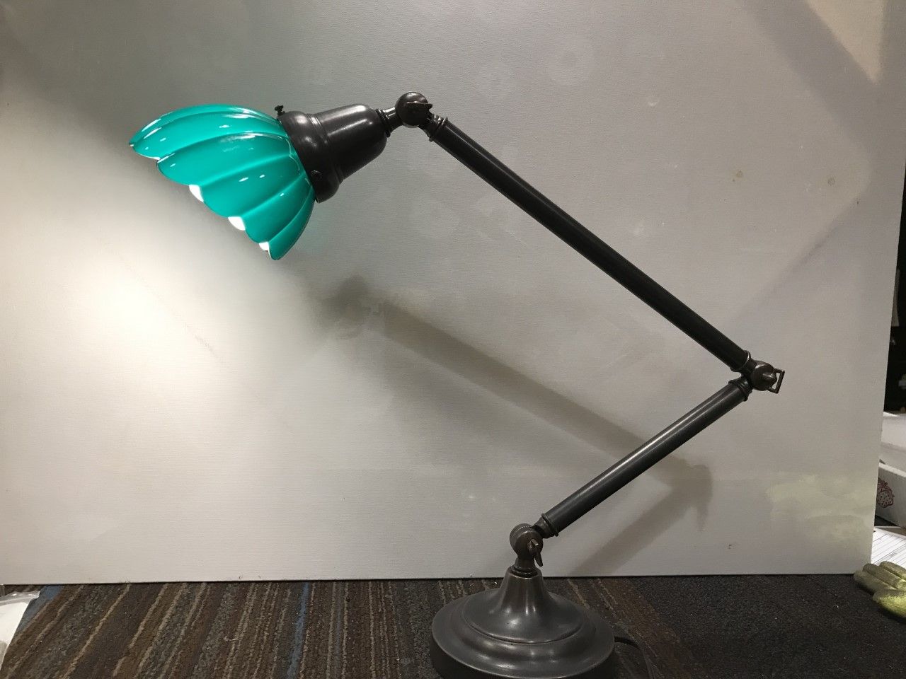 Green-shaded articulated desk lamp on a black base, illuminating a plain wall.