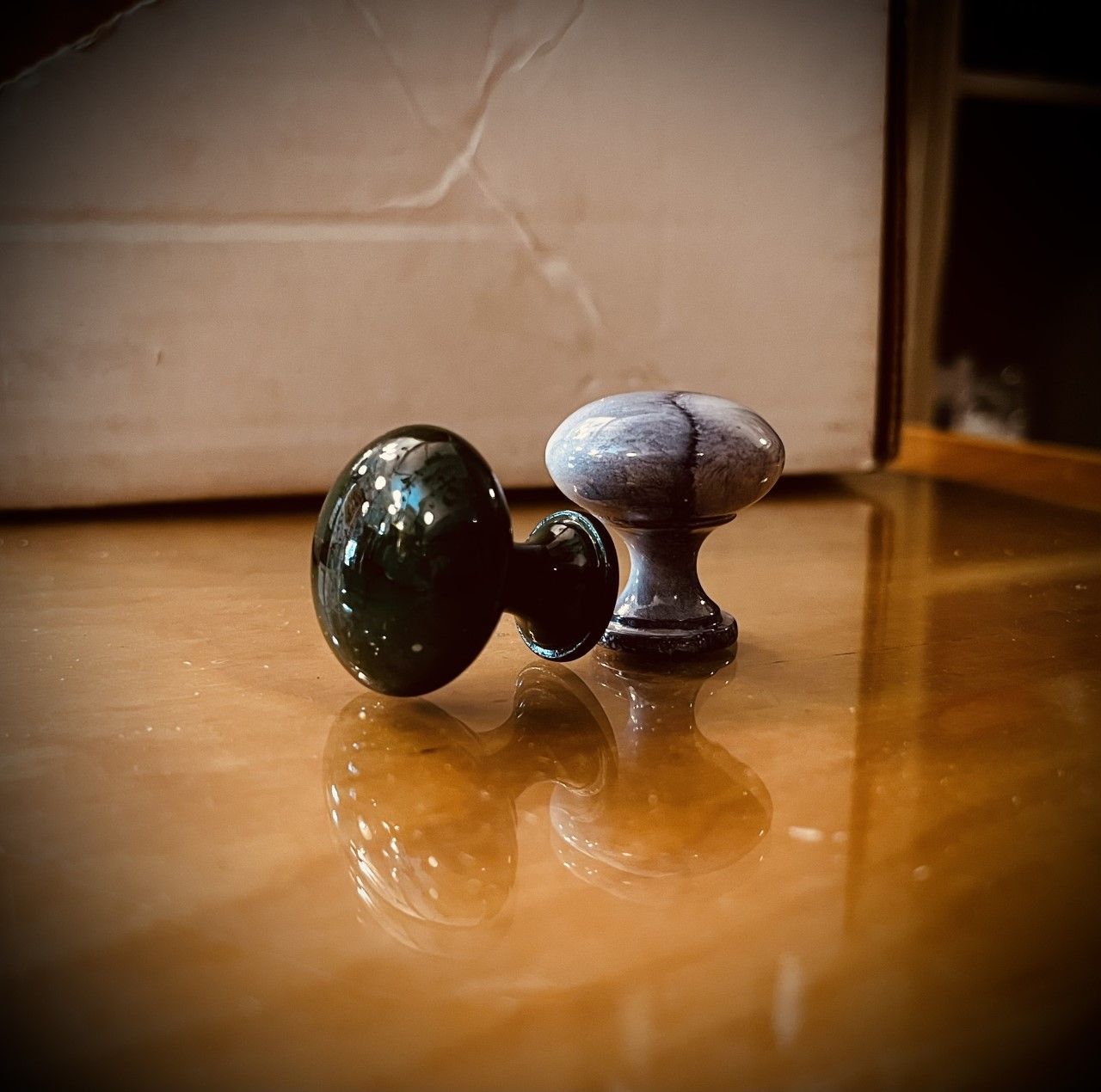 Two antique doorknobs on a reflective wooden surface, one dark green and one gray.