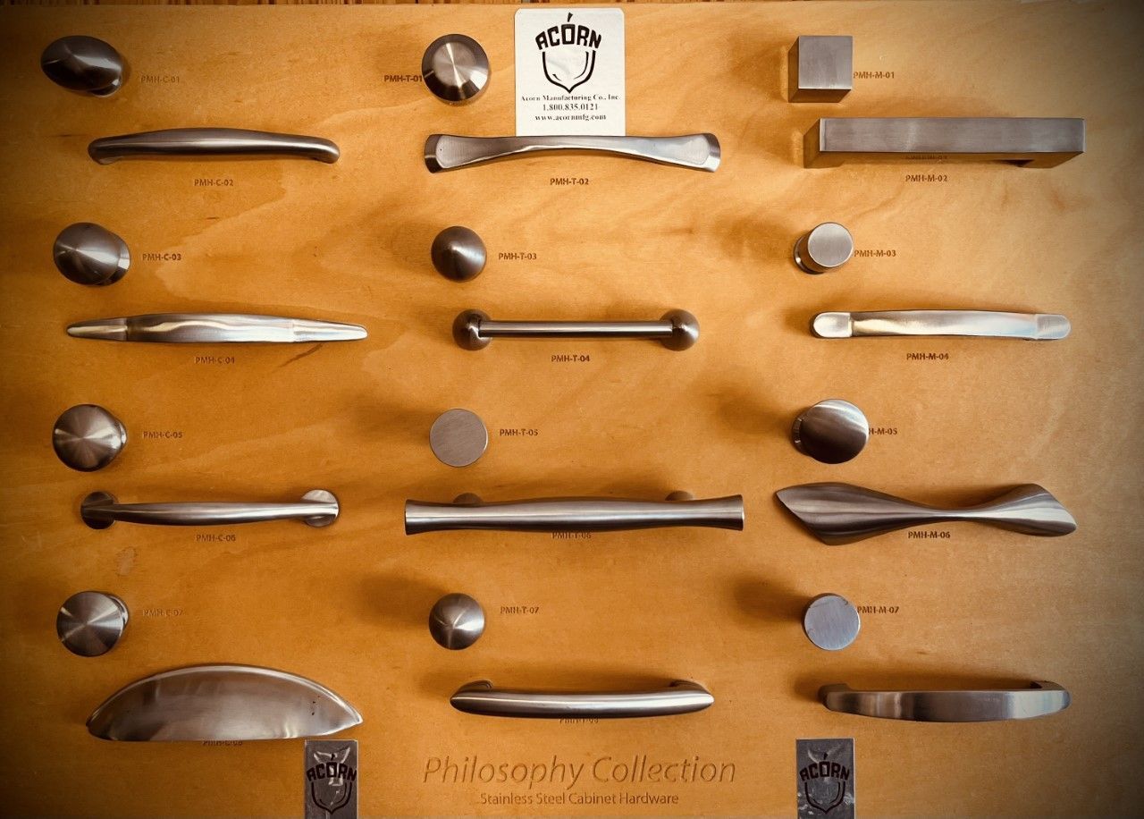 Display board of various metal cabinet pulls and knobs, arranged on a wood surface.