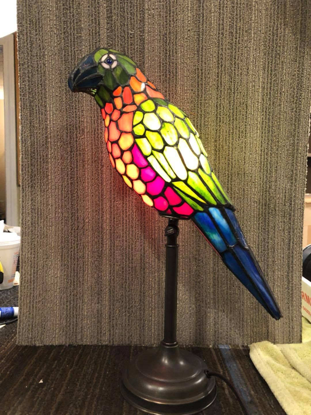 Stained glass parrot lamp in vibrant colors atop a dark metal stand on a table.