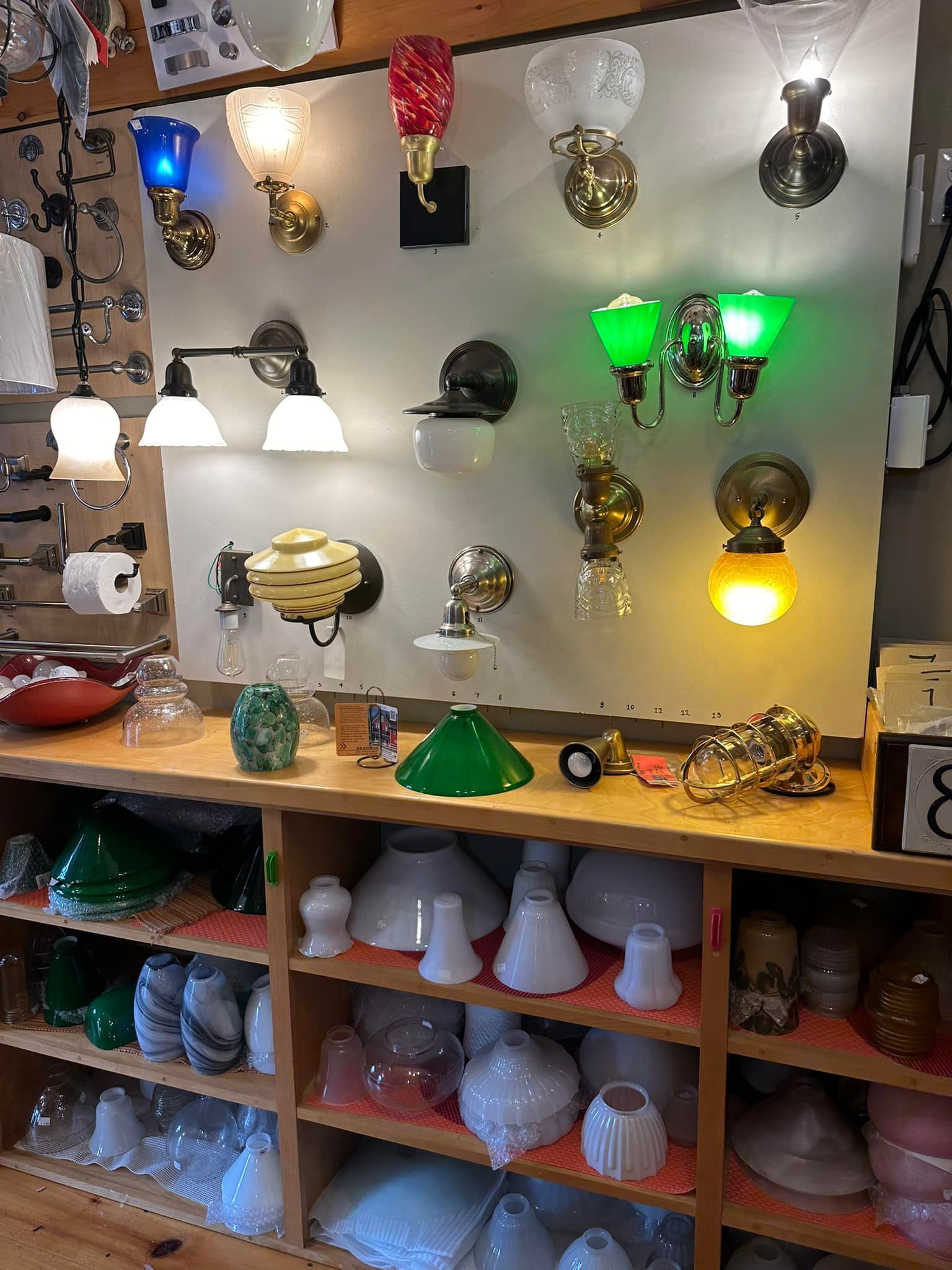 Wall sconces and lampshades displayed on a shelf in a store, lit in various colors.