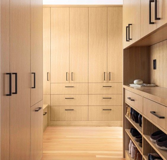 Walk-in closet with light wood cabinets, black hardware, and shoe shelves.