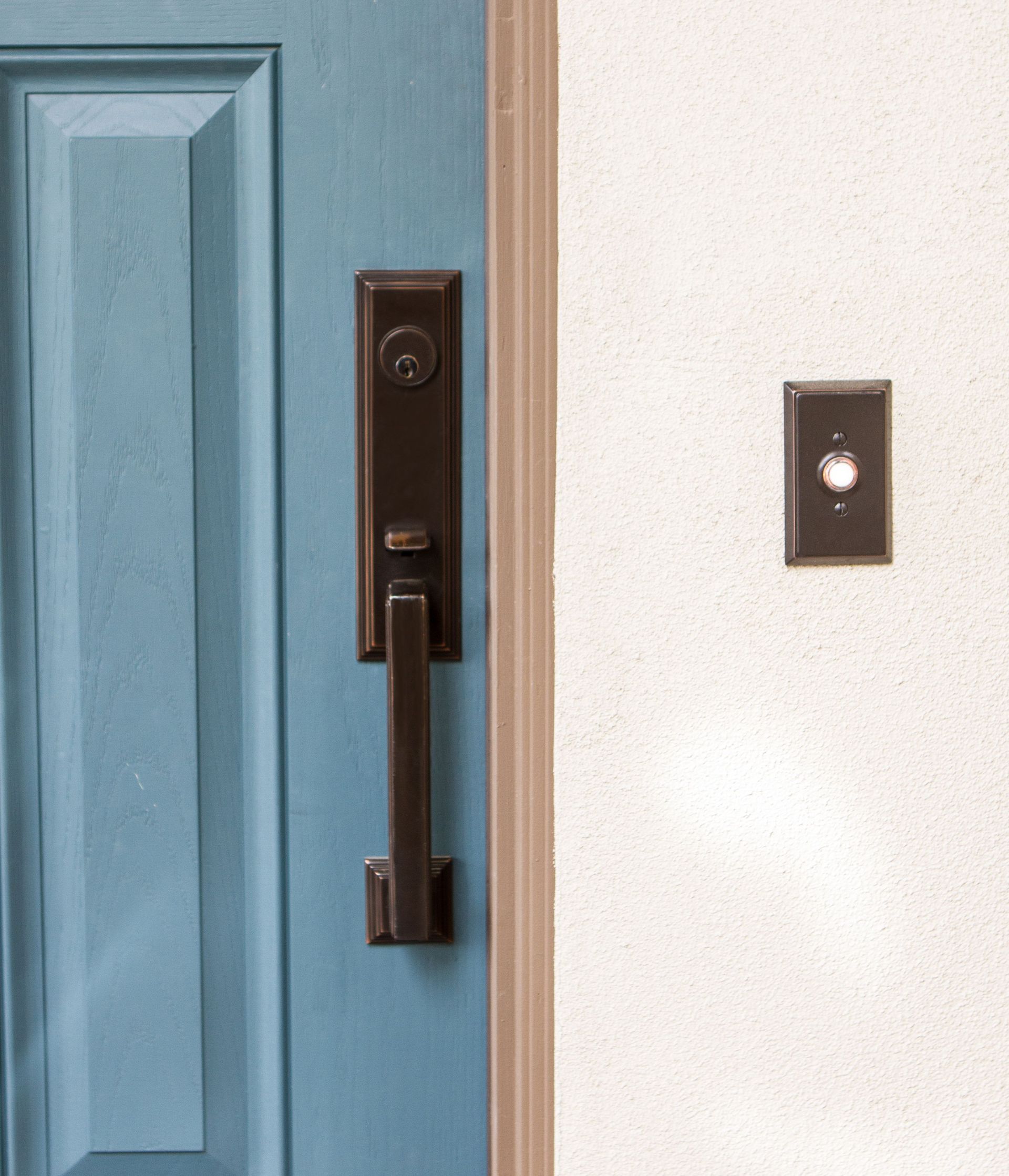 Blue door with dark bronze handle and doorbell on a white wall.