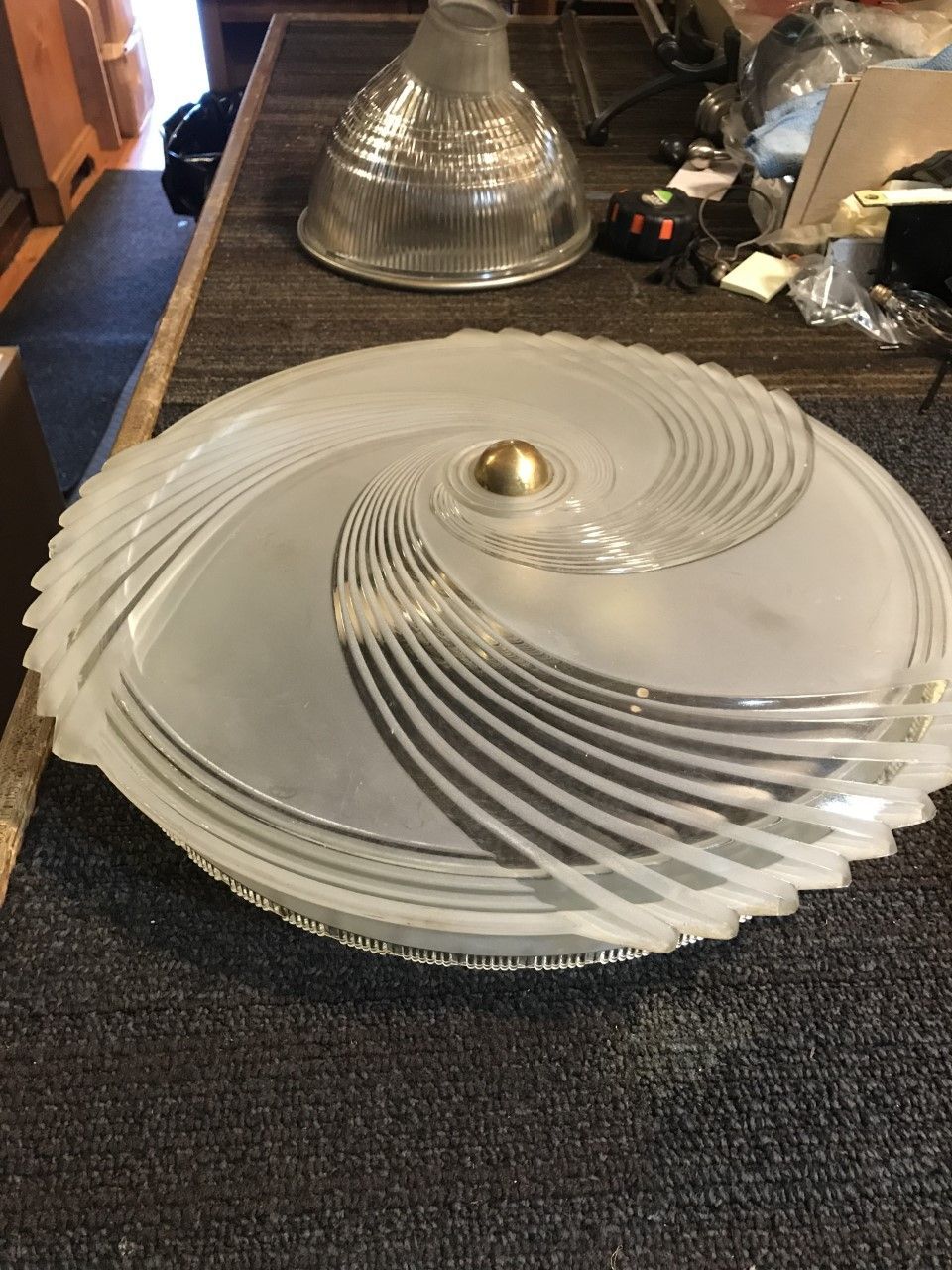 Circular frosted glass light fixture with swirl design, gold center, resting on a table.