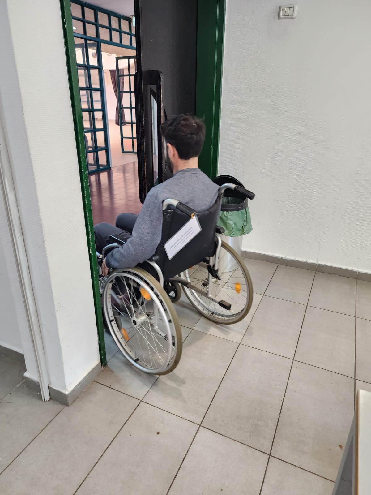אדם בכיסא גלגלים ממתין בפתח בתוך מסדרון מרוצף
