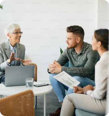 A woman is talking to a man and a woman while sitting at a table with a laptop.