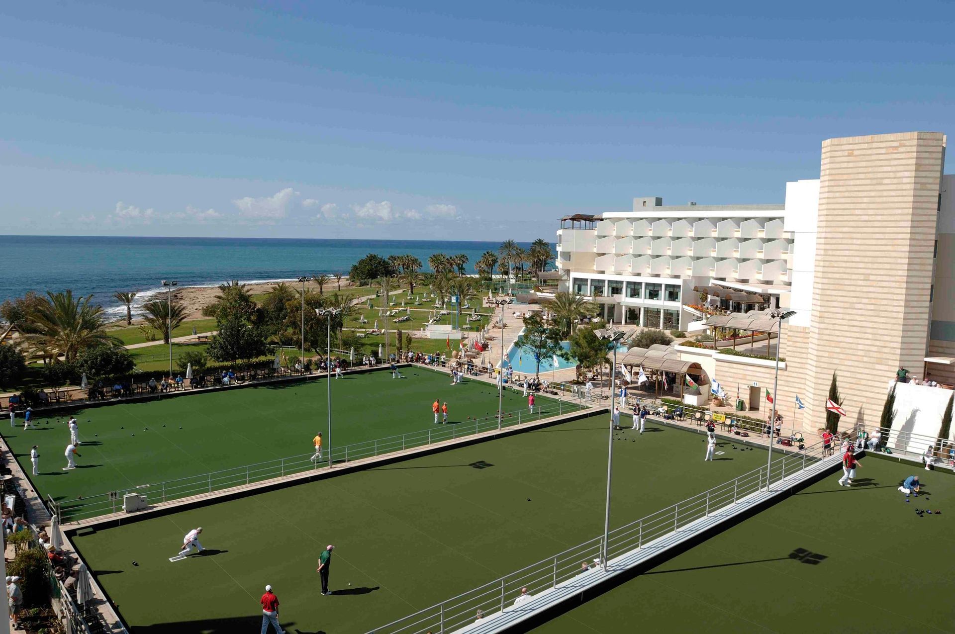 Bowls Holidays. A group of people are playing lawn bowling in front of a large building.