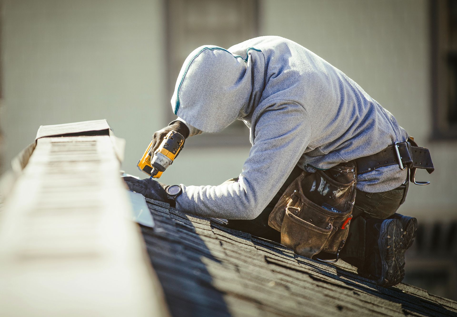 Roofer from a residential roof company using a drill to secure shingles on a home.