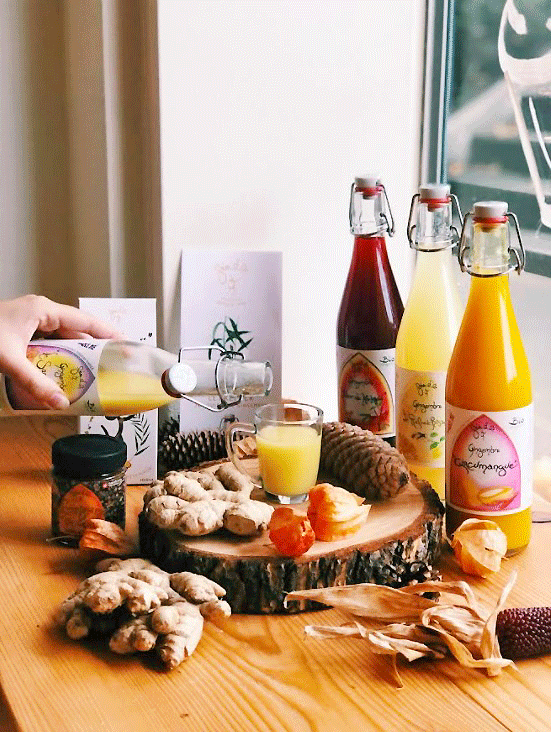 Jus de fruits variés et racines de gingembre sur une table en bois, une main versant du jus dans un verre