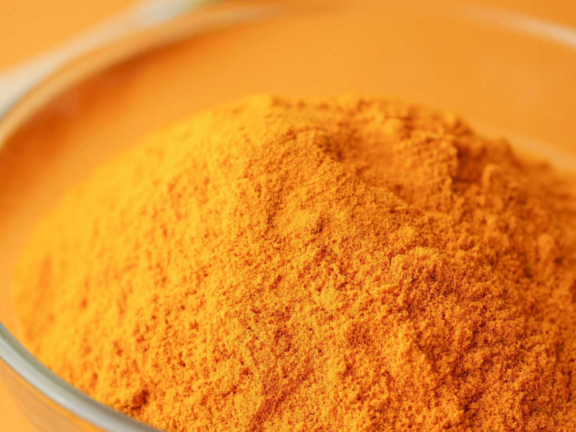 Gros plan sur une épice en poudre orange vif dans un bol en verre