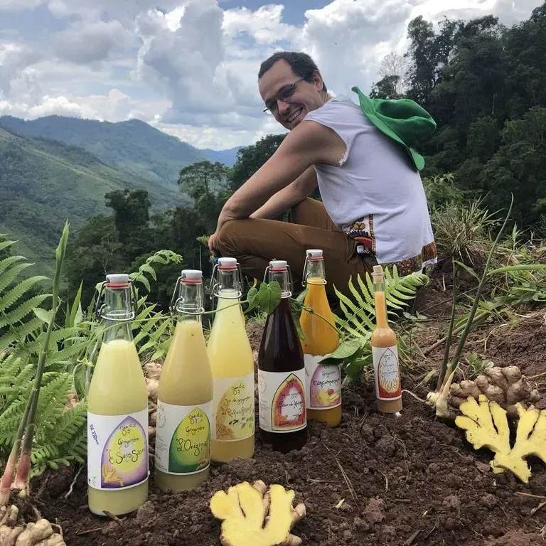 Une personne sur une colline avec des bouteilles de jus et des fruits étalés devant une vue sur la montagne