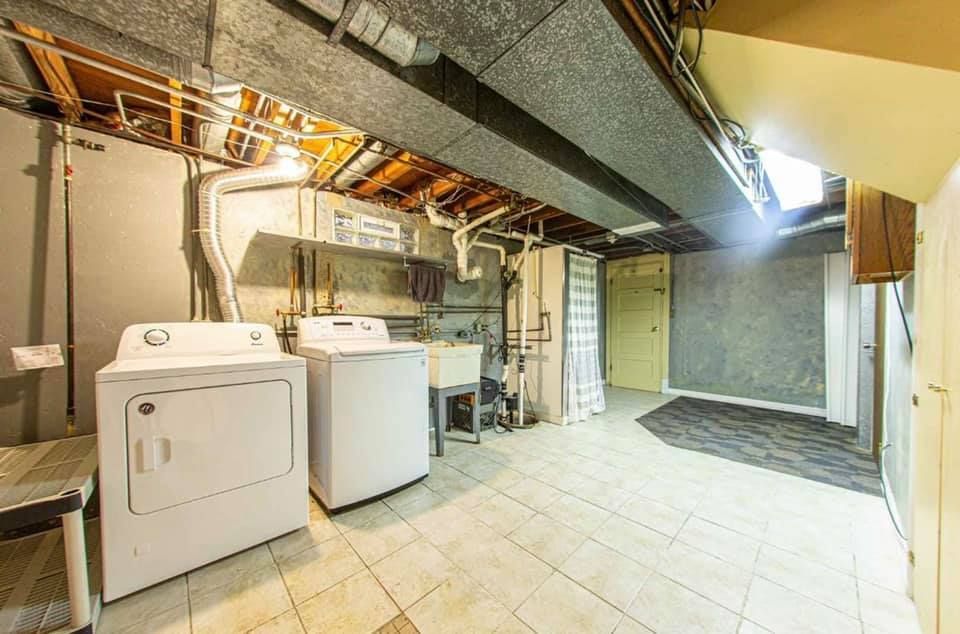 A residential basement laundry area featuring white washer and dryer units, a utility sink, and unfinished ceilings.