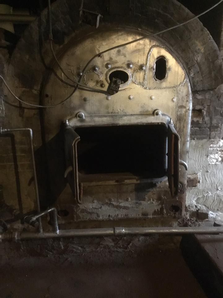 An old, industrial-style furnace or boiler with a large, open metal door, set within a rustic masonry structure.