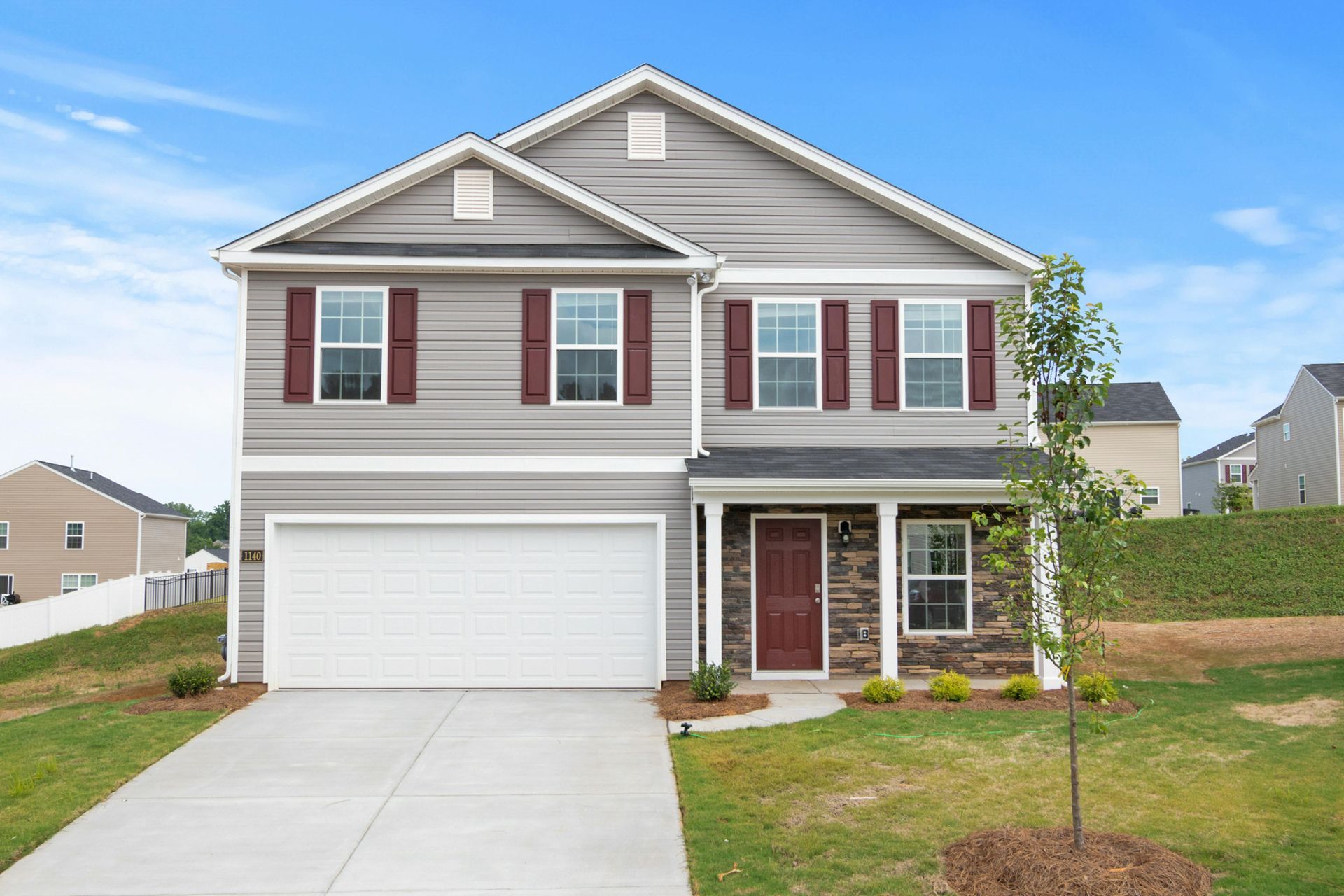 A two-story suburban house with grey siding, a white garage door, a dark red front door, and a stone facade entry.