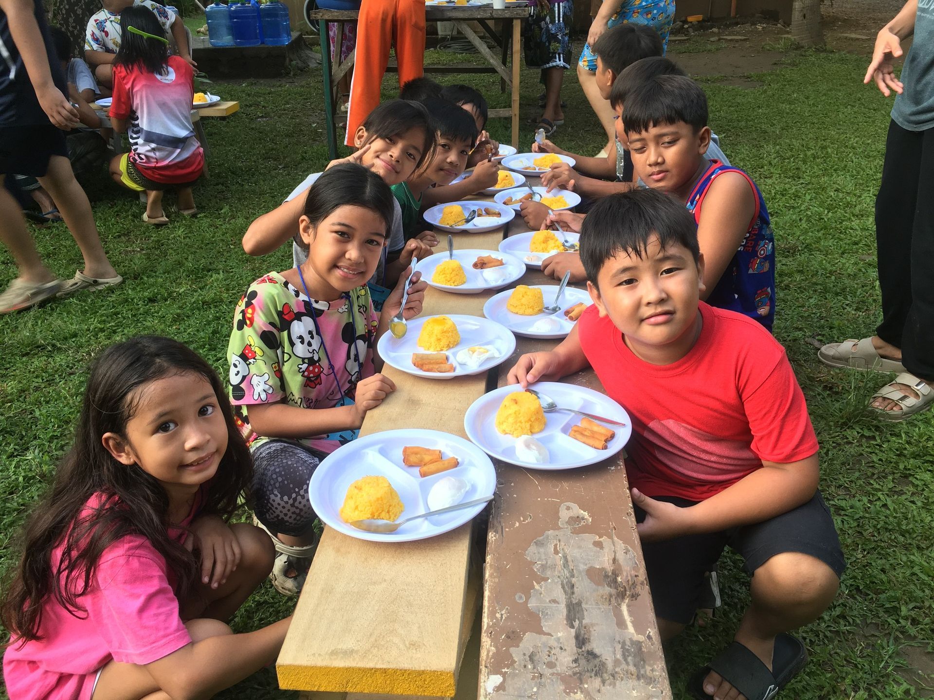 A group of children are sitting at a table with plates of food.