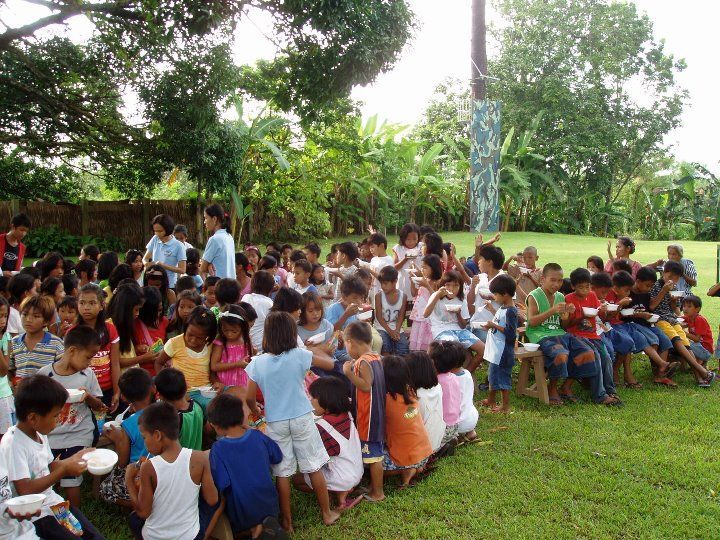 A large group of children are sitting on the grass eating food