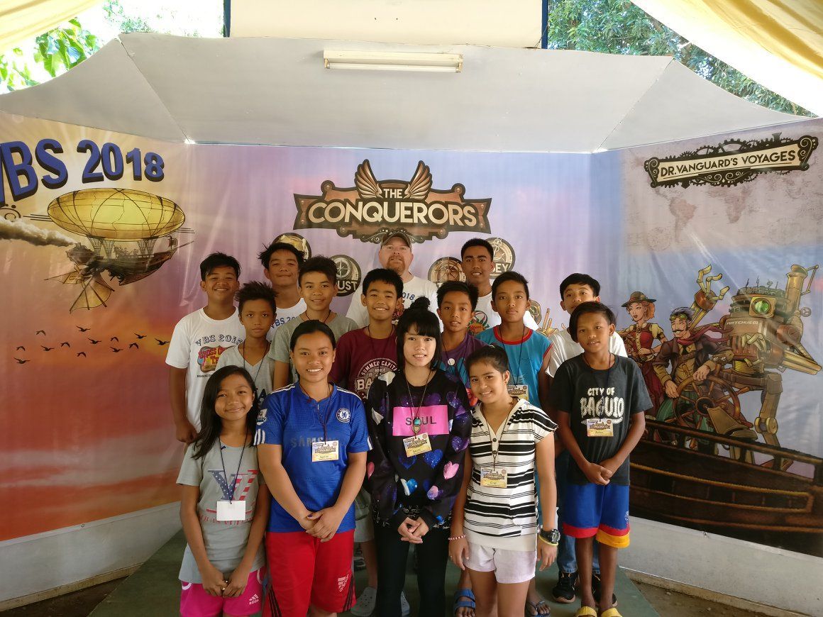 A group of children are posing for a picture in front of a sign that says conquerors