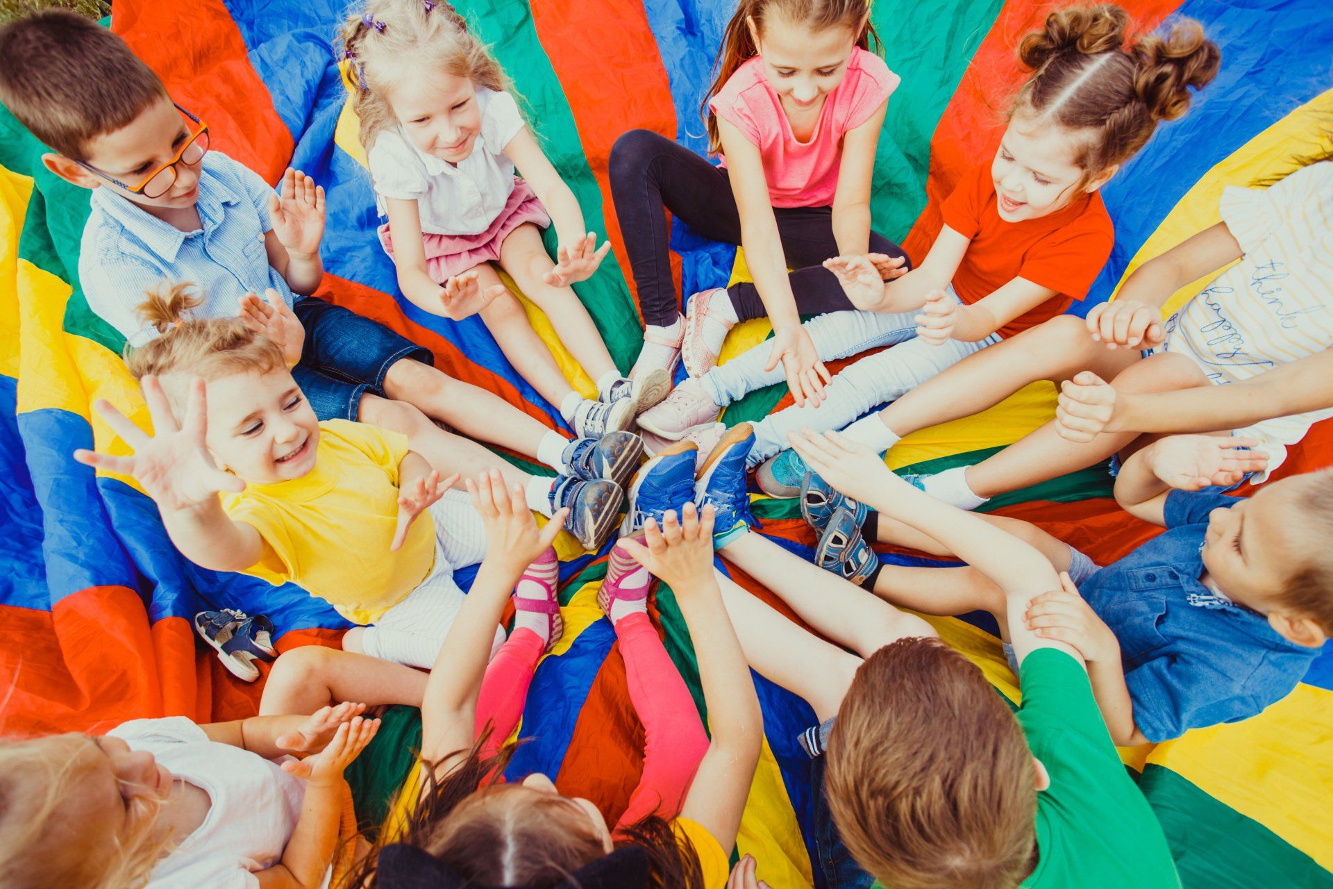 Eine Gruppe Kinder sitzt im Kreis auf einem bunten Fallschirm.