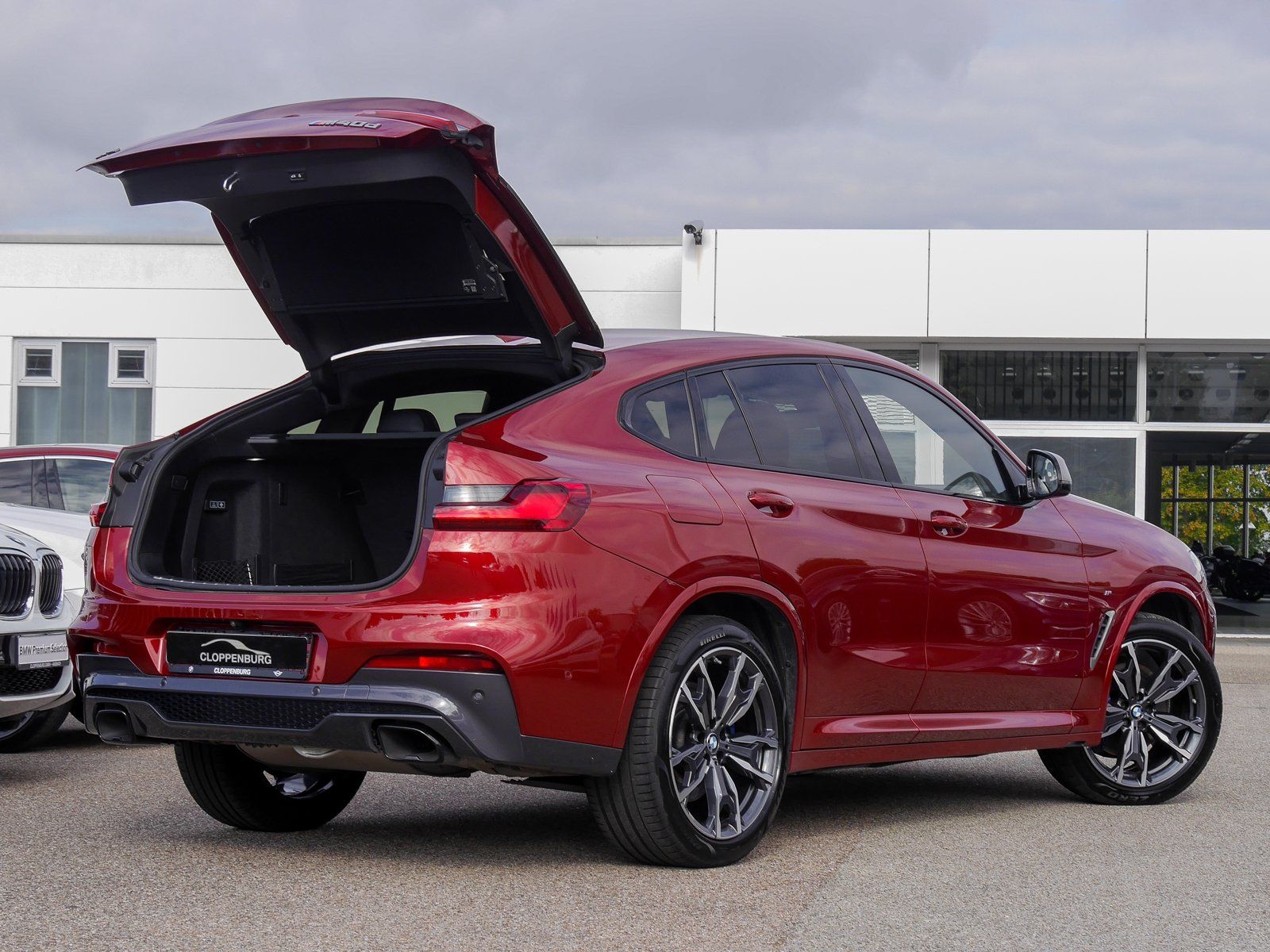 Vor einem Gebäude parkt ein roter BMW X4 mit geöffnetem Kofferraum.