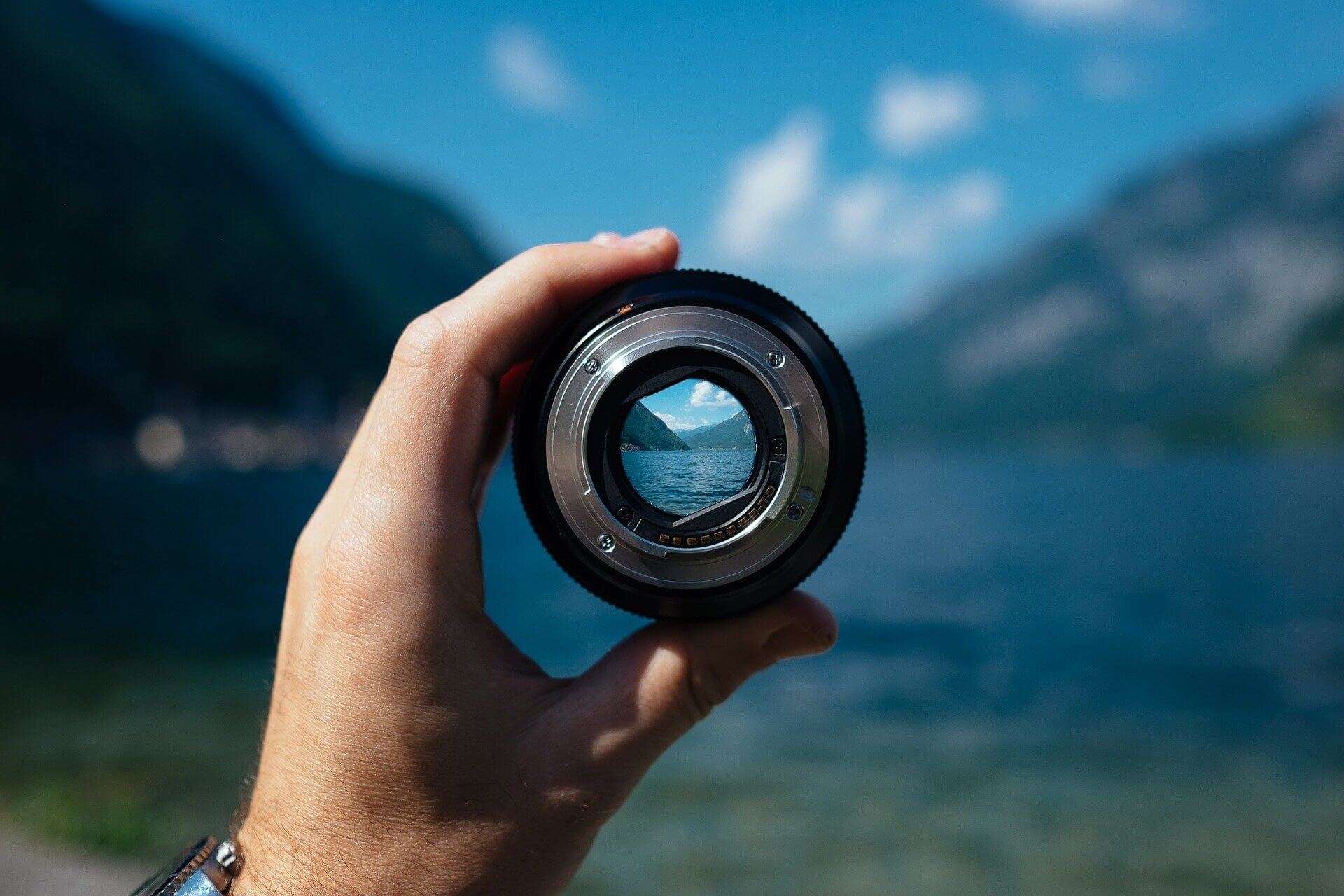 Eine Person hält ein Kameraobjektiv vor einem See.