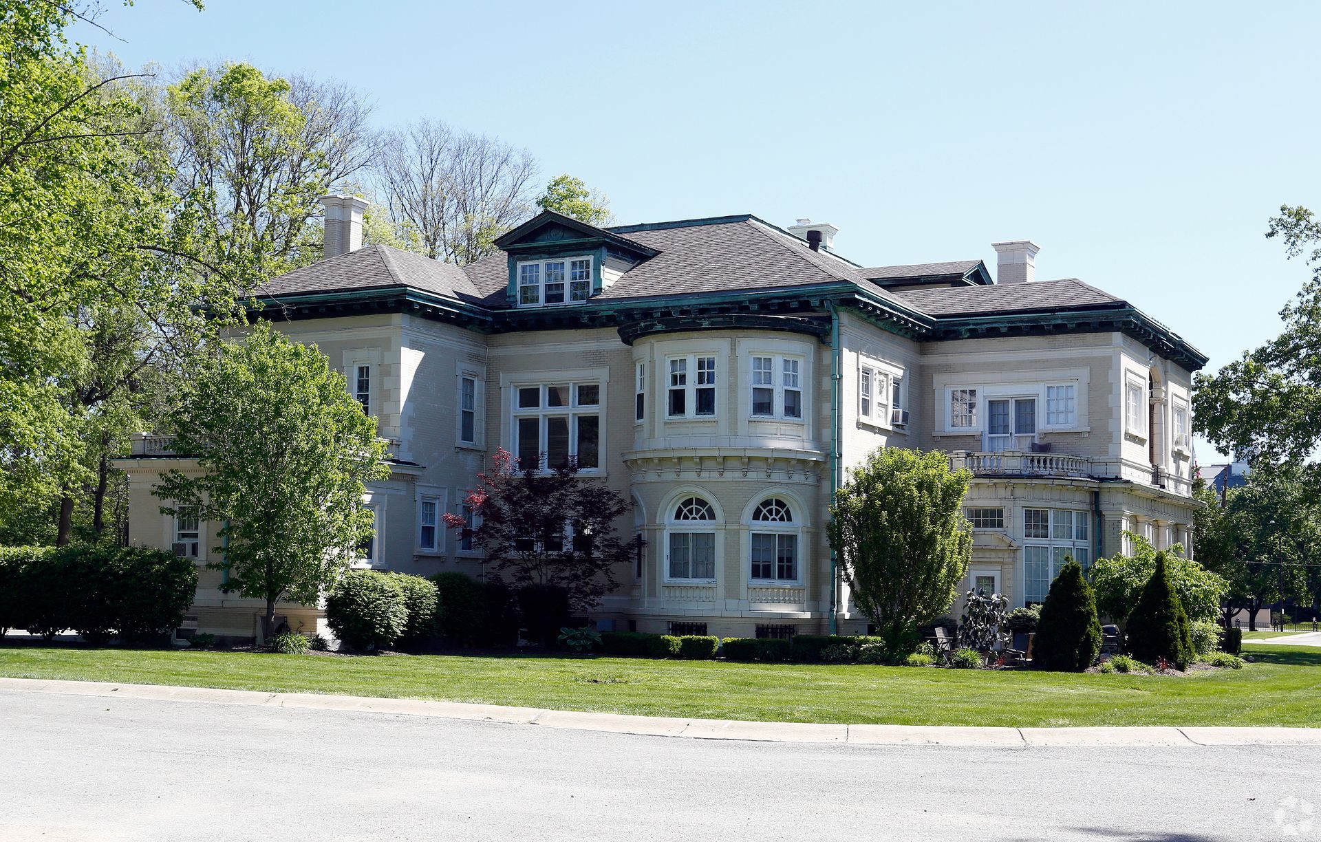 A large white house with a gray roof is surrounded by trees