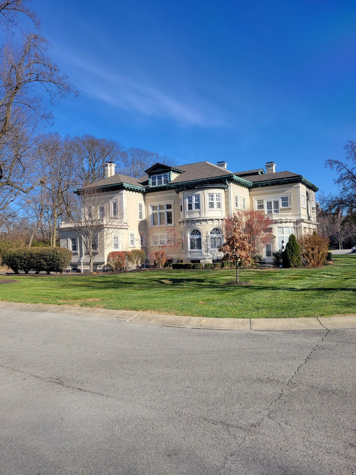 A large white house with a green roof is sitting on top of a lush green field.