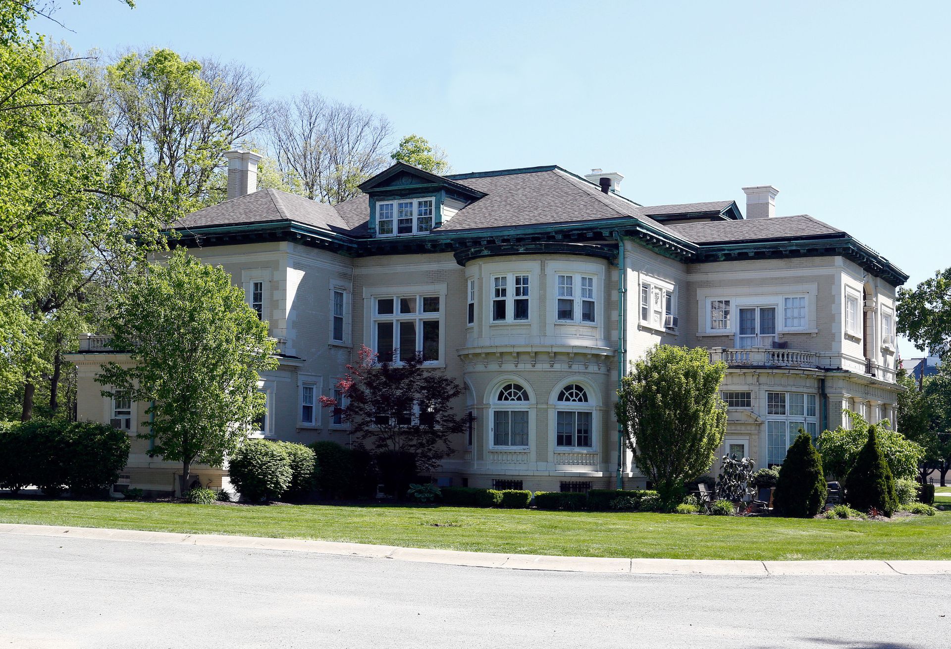 A large white house is surrounded by trees and grass