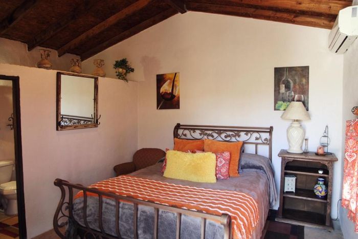 Habitación acogedora con cama de metal, ropa de cama a rayas, vigas de madera, cuadros en la pared y lámpara de noche.